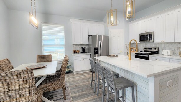A modern kitchen with white cabinetry, stainless steel appliances, and a central island with bar stools. - BELLE VUE- Pristine Bay Views - Community Pool (Galveston)