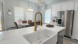 A modern kitchen with a white marble countertop, stainless steel appliances, and a gold faucet. - BELLE VUE- Pristine Bay Views - Community Pool (Galveston)