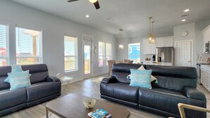 A spacious living room with two black leather sofas, a coffee table, and a dining area with a kitchen in the background. - BELLE VUE- Pristine Bay Views - Community Pool (Galveston)