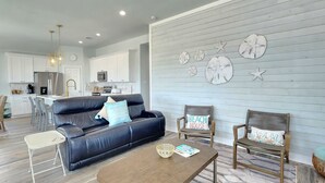 A modern living room with a black leather sofa, two wooden chairs, a coffee table, and a kitchen in the background. - BELLE VUE- Pristine Bay Views - Community Pool (Galveston)