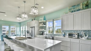 A modern kitchen with a large island, white cabinetry, and pendant lighting. - Seabatical! Home with private pool in Pointe West (Galveston)