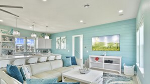 A modern living room with a sofa, coffee table, and a TV mounted on the wall. - Seabatical! Home with private pool in Pointe West (Galveston)
