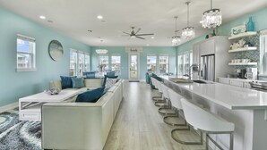 A modern kitchen with a central island, bar seating, and a view to the dining area. - Seabatical! Home with private pool in Pointe West (Galveston)