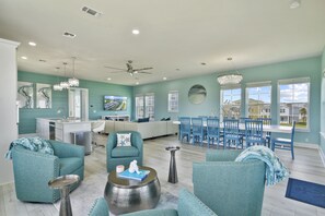 A spacious living area with teal-colored furniture, a dining table with blue chairs, and a kitchen area in the background.