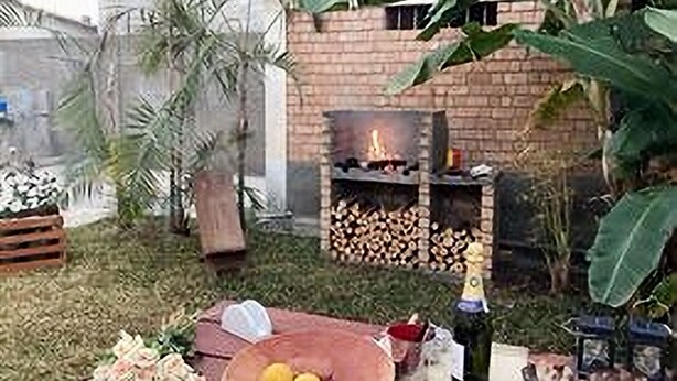 An outdoor patio with a brick wall, a wood-burning stove, and a dining setup with a bottle of champagne, lemons, and a bowl. - Villa ChezSoa Andoharanofotsy (ANTANANARIVO)