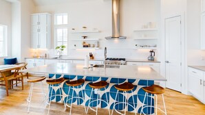 Une cuisine moderne avec des meubles blancs, un îlot central doté de tabourets de bar et une hotte de cuisine en acier inoxydable.