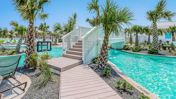 Un espace piscine doté d’une terrasse en bois, de palmiers et d’un escalier menant à un bâtiment.