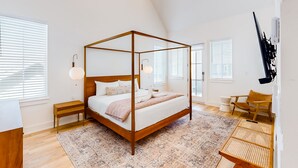 Une chambre spacieuse avec un lit à baldaquin, un banc en bois et une table d’appoint en rotin.