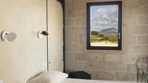 Un dormitorio con una cama grande, una ventana con vistas a una playa y una pared de ladrillo.