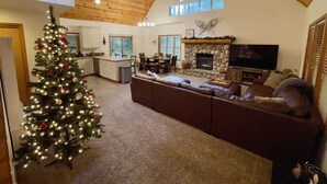 A cozy living room with a fireplace, a large TV, and a Christmas tree. - Cozy Cascade Cabin. Relaxing Hot Tub, Secluded, Spacious and Creek Nearby (Rhododendron)