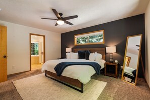 A bedroom with a bed, a ceiling fan, a window, a nightstand, and a mirror. - Cozy Cascade Cabin. Relaxing Hot Tub, Spacious and Creek Nearby (Rhododendron)