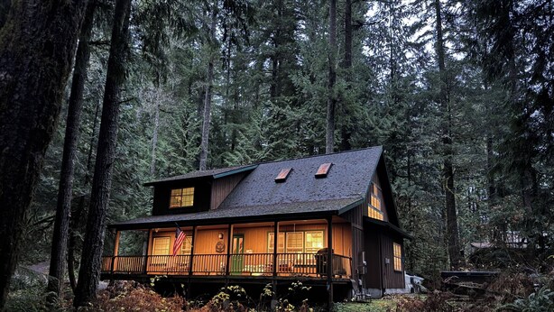 A cabin with a wooden exterior, large windows, and a porch area. - Cozy Cascade Cabin. Relaxing Hot Tub, Secluded, Spacious and Creek Nearby (Rhododendron)