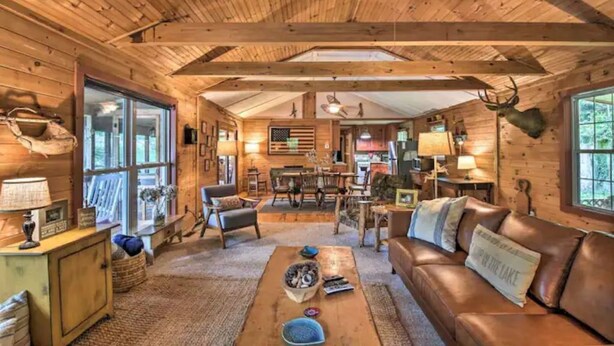 Interior acogedor de una cabaña con paredes de madera, un sofá de cuero, zona de comedor y una cornamenta de venado colgada.