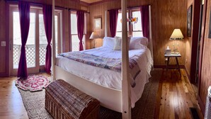 Un dormitorio con piso de madera, una cama, una mesita de noche, una lámpara y una ventana con cortinas.
