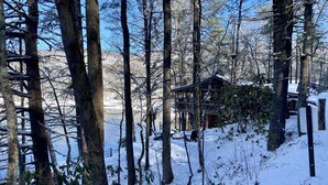 Una cabaña rodeada de árboles altos y suelo cubierto de nieve.