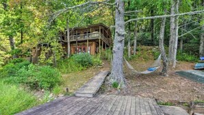 Una cabaña rústica con terraza de madera, rodeada de un bosque denso.
