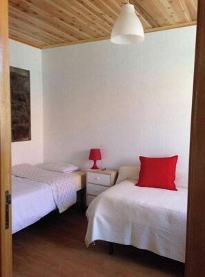 A bedroom with two beds, a wooden ceiling, and a white pendant light.