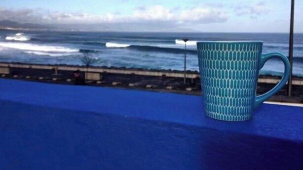 A teal mug on a blue surface with a view of the ocean and a cloudy sky. - House (Ribeira Grande)