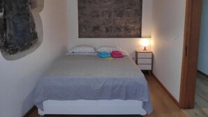 A bedroom with a bed, a nightstand, a wall-mounted painting, and a wooden ceiling. - House (Ribeira Grande)
