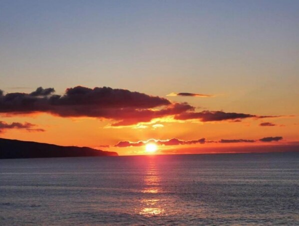 A sunset over a calm sea with a silhouette of a landmass in the distance.