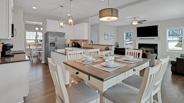A modern kitchen with white cabinetry, a central island, and a dining area with a wooden table and white chairs. - Spacious 4 BD Golf Getaway with Game Room! (Aberdeen)