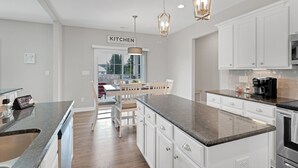 A modern kitchen with white cabinetry, granite countertops, and stainless steel appliances. There is a dining area with a table and chairs visible through the window. - Spacious 4 BD Golf Getaway with Game Room! (Aberdeen)