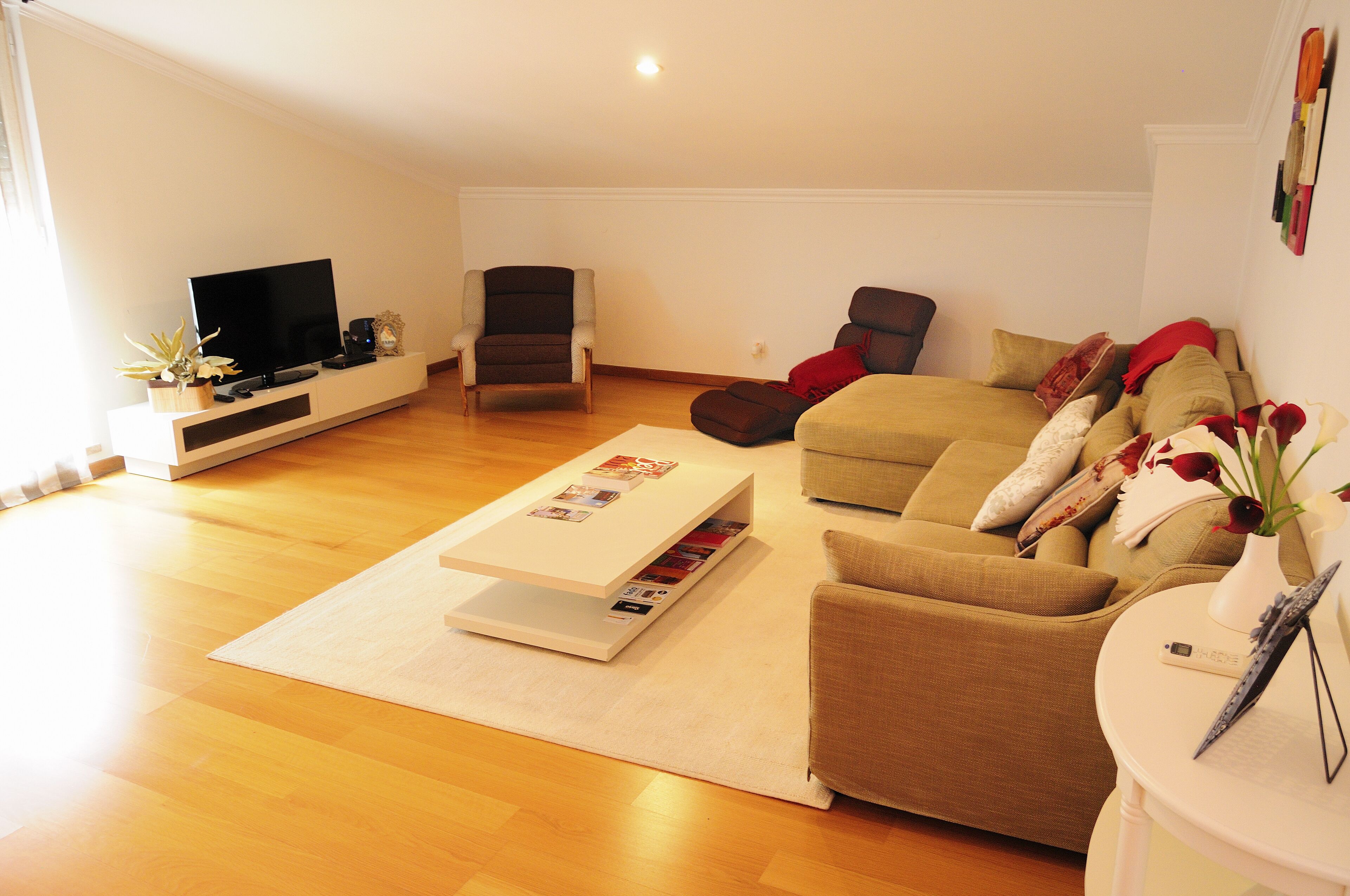 A living room with a flat-screen TV, a sofa, a coffee table, and a small side table with a vase.