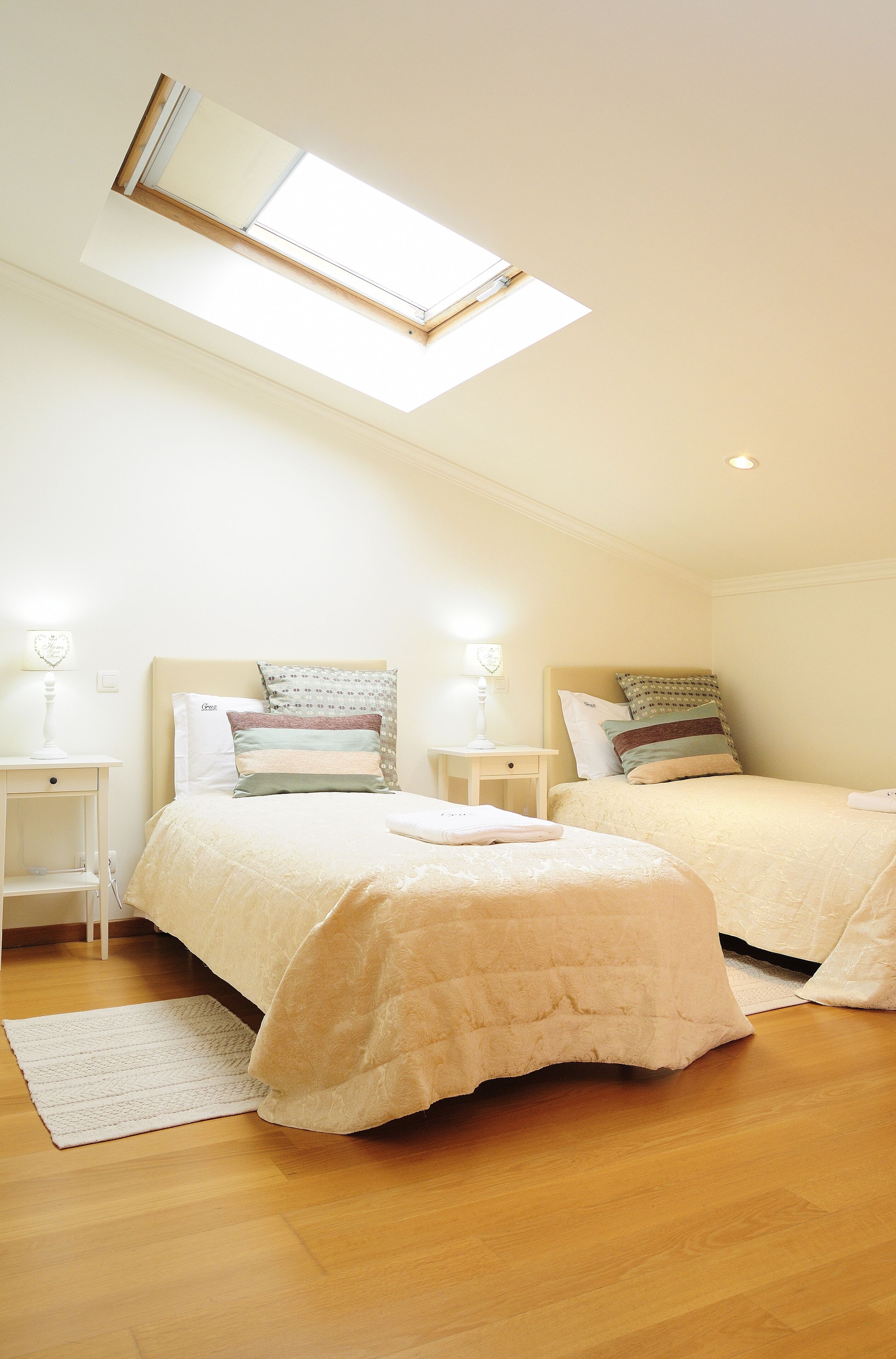 Een slaapkamer met twee bedden, een dakraam, nachtkastjes en een houten vloer.