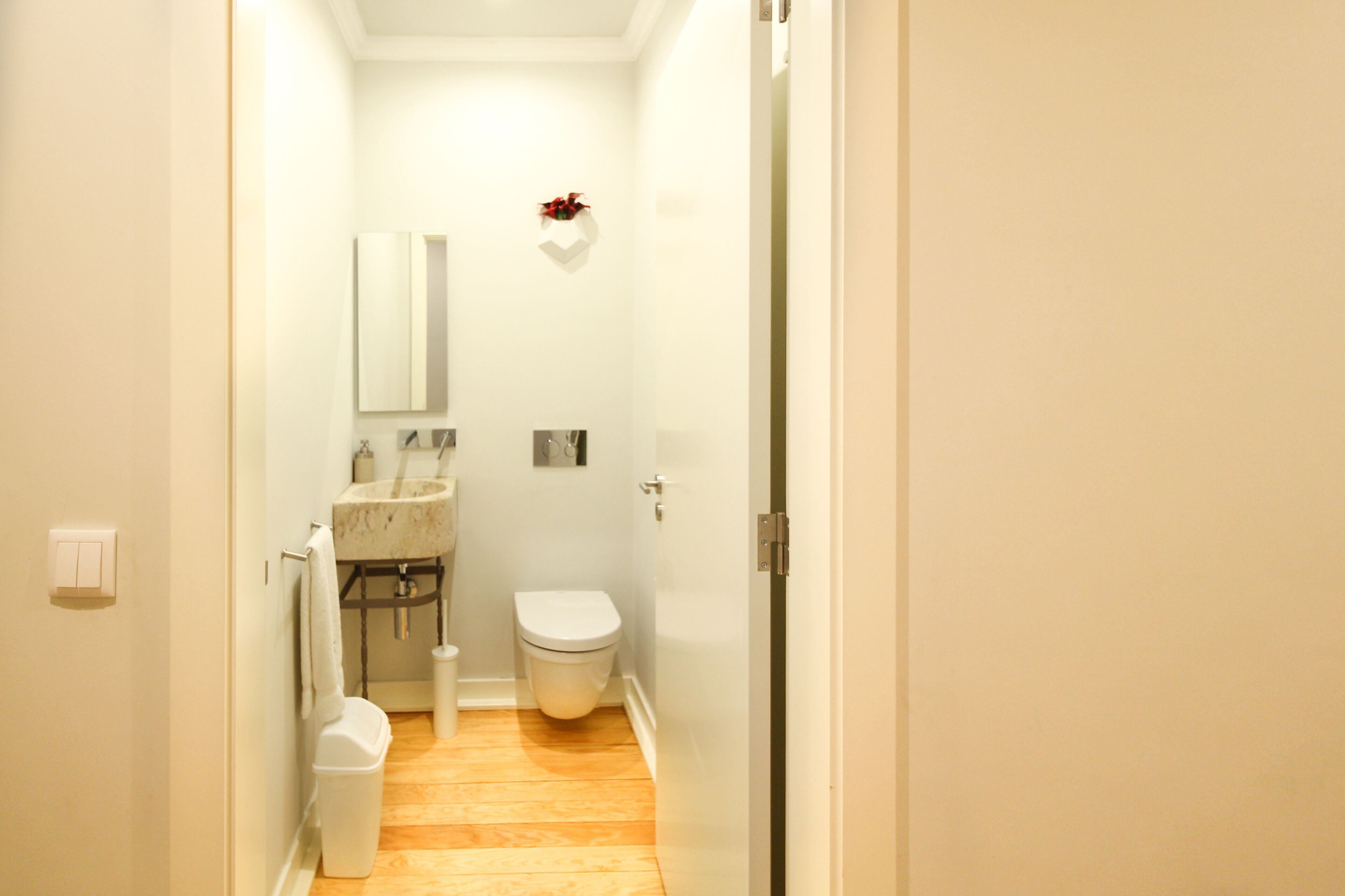 A narrow hallway leading to a bathroom with a toilet, sink, and mirror.