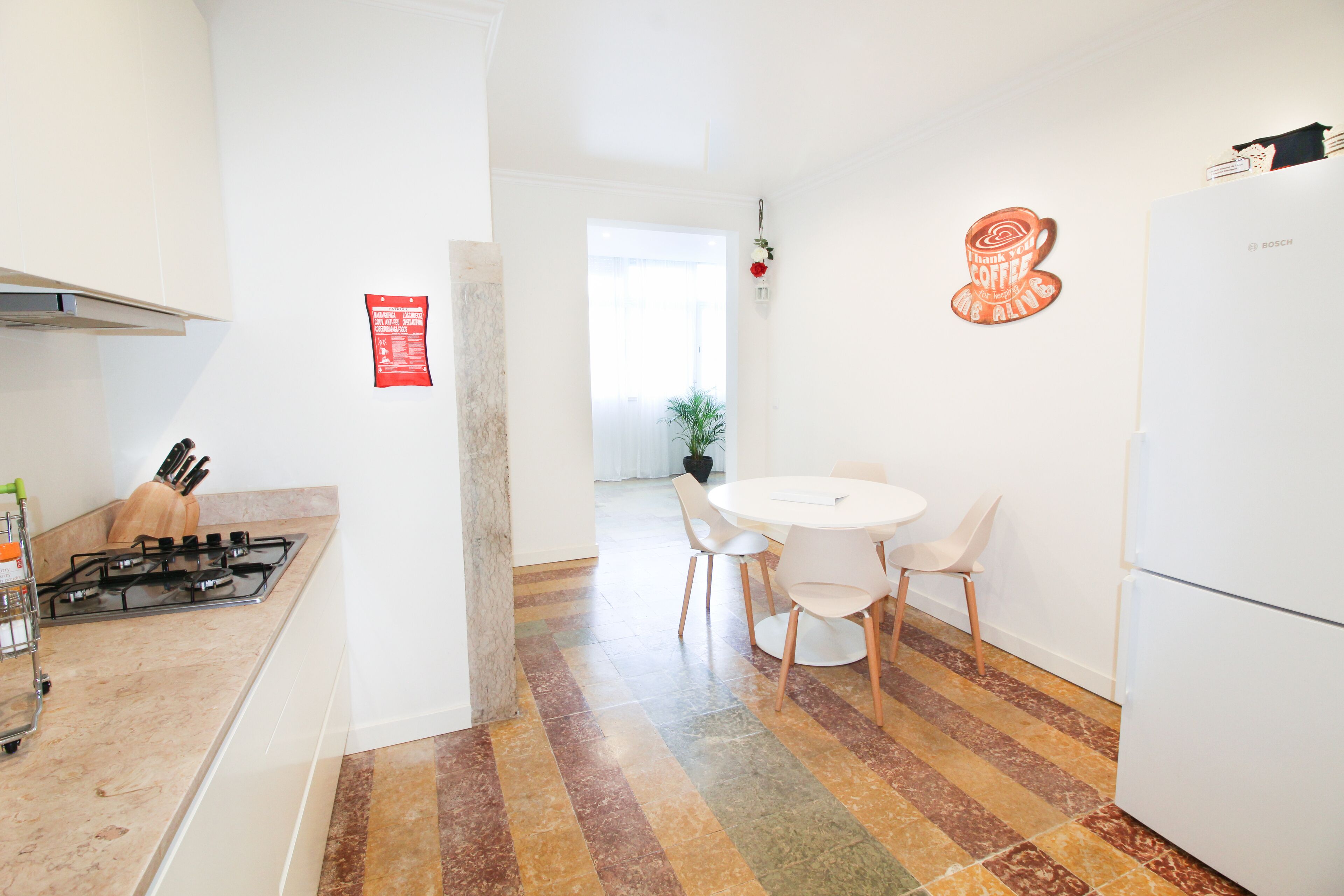 A modern kitchen with a gas stove, white cabinets, a refrigerator, and a dining area with a table and chairs.