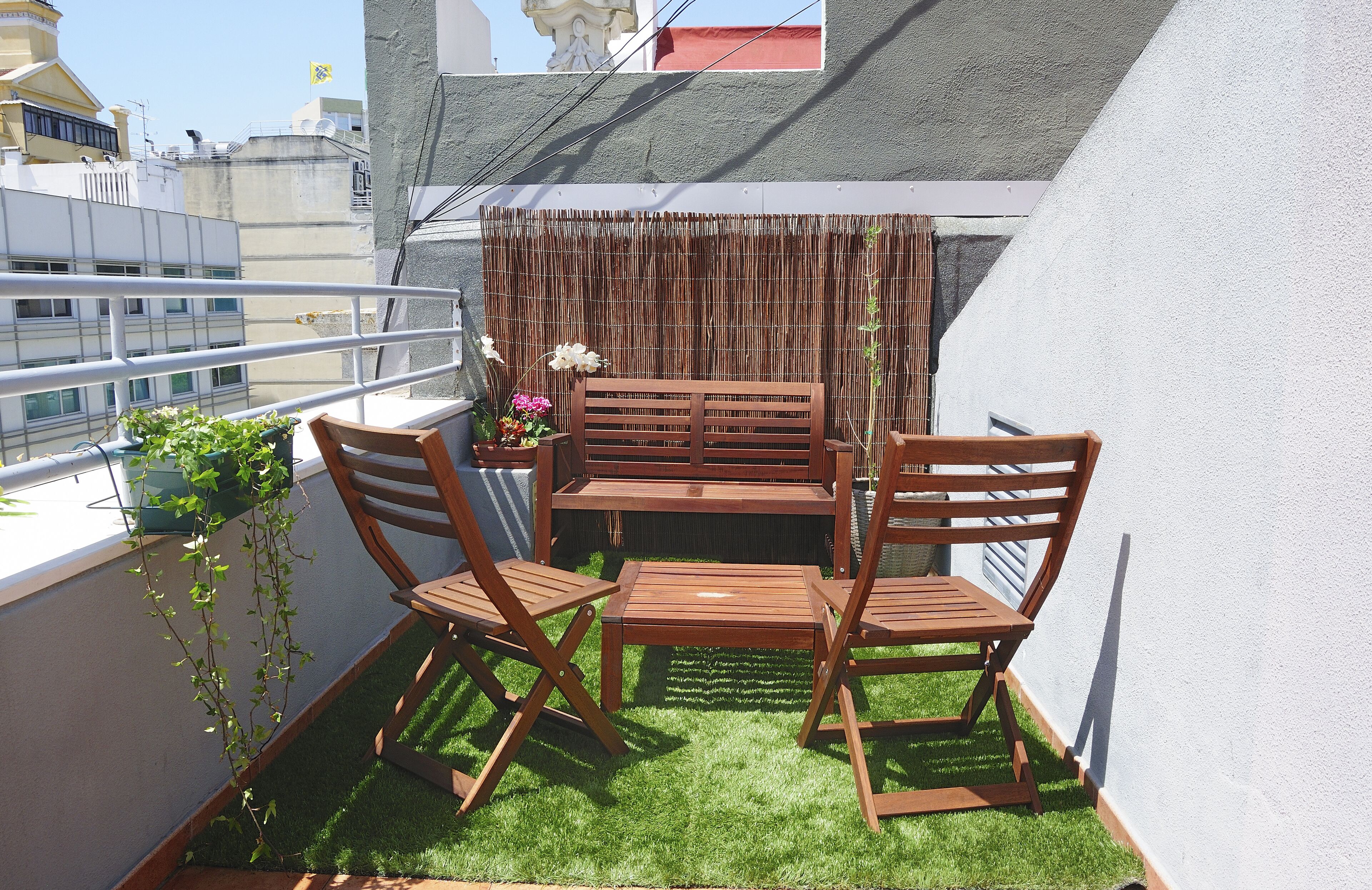 A small balcony with a wooden table and chairs, a bamboo screen, and potted plants.