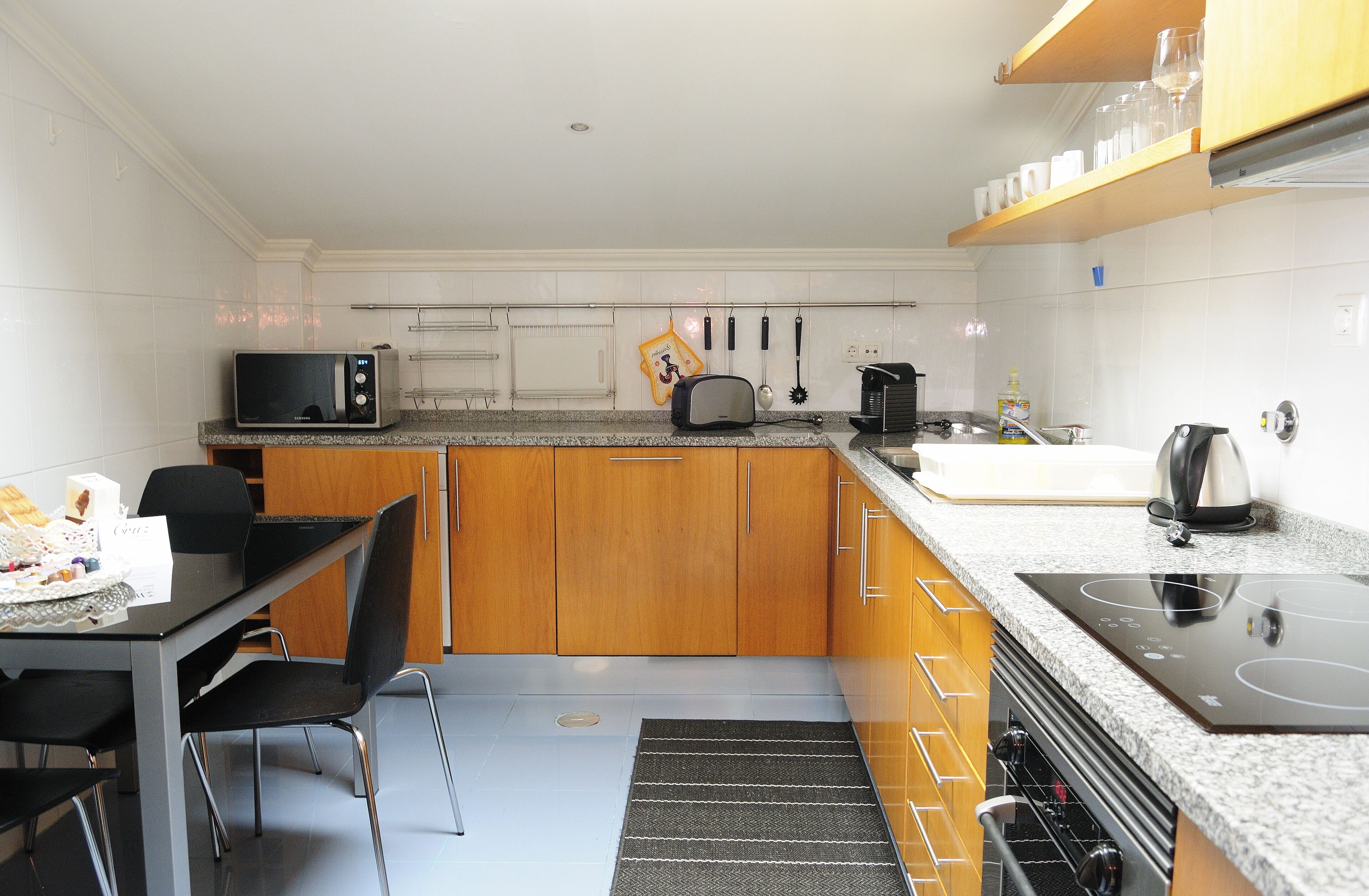 A compact kitchen with a microwave, toaster, kettle, and built-in oven. There is a dining table with chairs and a small rug.