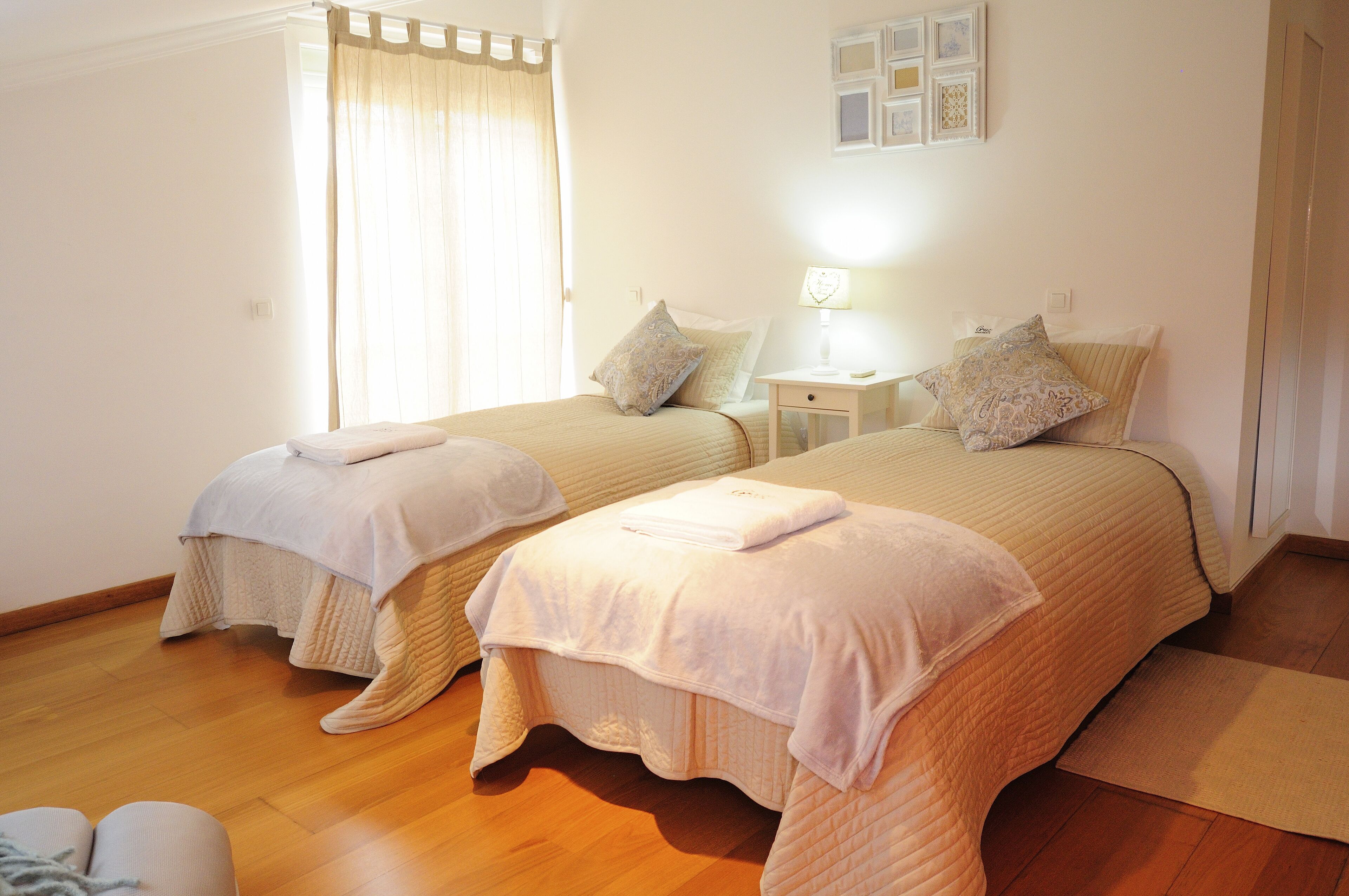 A bedroom with two beds, a nightstand, a lamp, and a window with curtains.