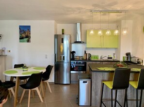 A modern kitchen with a stainless steel refrigerator, an oven, and a sink. There is a dining area with a round table and chairs.