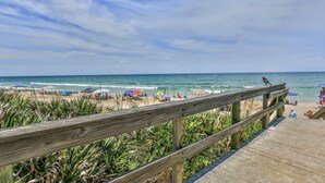Une promenade en bois menant à une plage où se trouvent des parasols et des gens.
