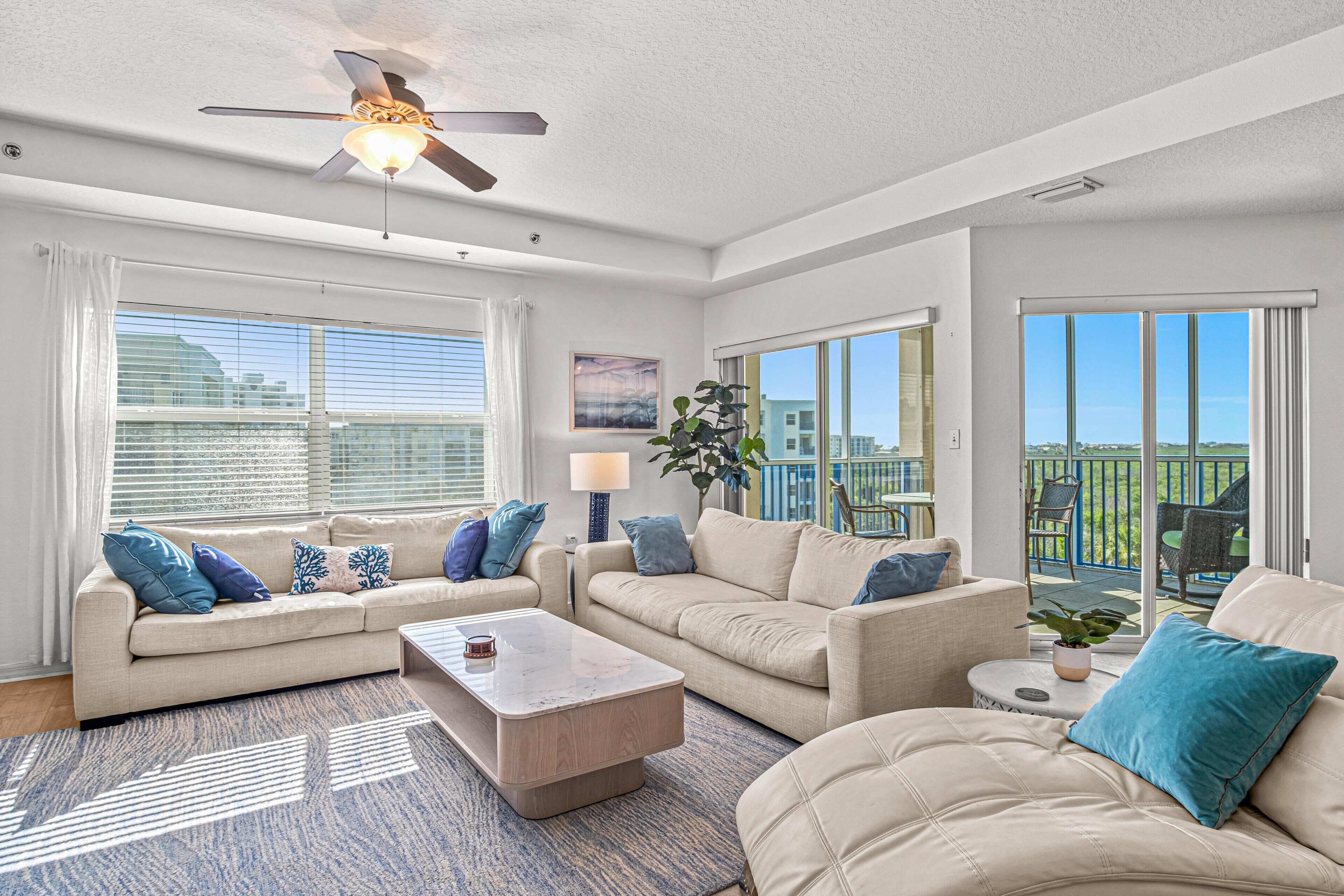 A spacious living room with a ceiling fan, large windows, and a balcony with outdoor furniture.