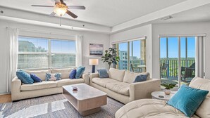 Un salon spacieux doté d’un ventilateur de plafond, de grandes fenêtres et d’un balcon aménagé avec du mobilier d’extérieur.