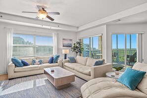 A spacious living room with a ceiling fan, large windows, and a balcony with outdoor furniture.