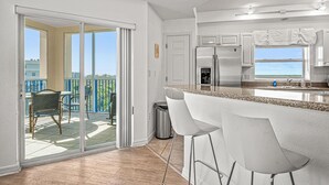 Une cuisine moderne dotée d’un grand îlot central, de tabourets de bar et d’une porte-fenêtre coulissante donnant sur un balcon.