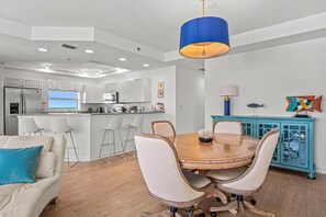 A modern kitchen with white cabinets, a dining area with a wooden table and chairs, and a blue pendant light.