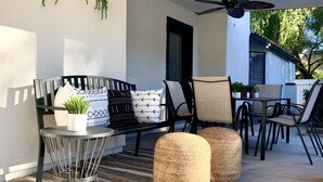 A covered patio with a black sofa, round table, and chairs, featuring woven ottomans and potted plants. - Beautiful 5-Bdrm Vacation Home W/Heated Pool ! (Scottsdale)