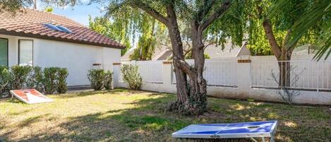 A residential backyard with a tree, a trampoline, and a house with a tiled roof.