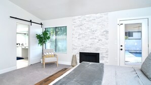 A bedroom with a bed, a fireplace, a stone wall, a door leading to a balcony, and a plant. - Beautiful 5-Bdrm Vacation Home W/Heated Pool ! (Scottsdale)