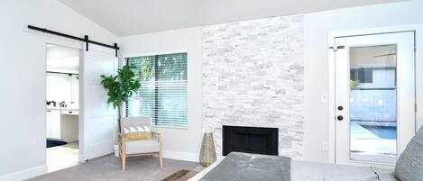 A bedroom with a bed, a fireplace, a stone wall, a door leading to a balcony, and a plant.