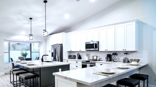 A modern kitchen with white cabinets, stainless steel appliances, and a large island with bar stools. - Beautiful 5-Bdrm Vacation Home W/Heated Pool ! (Scottsdale)