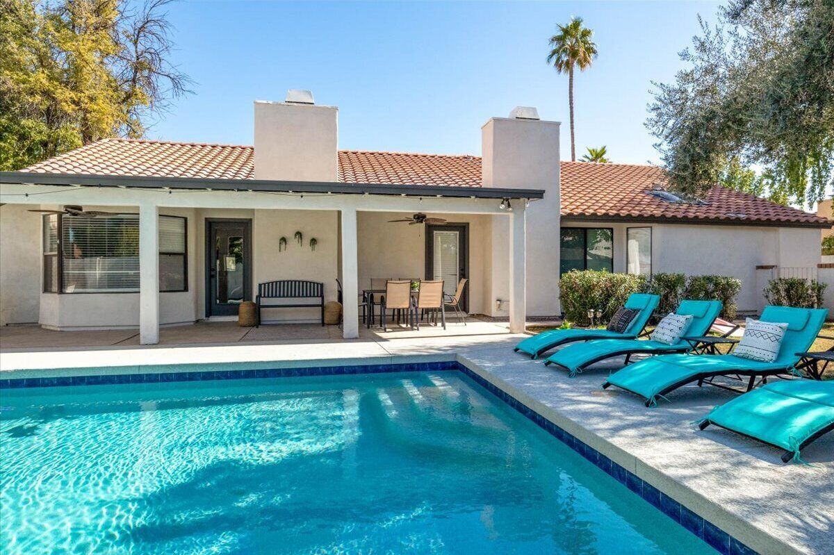 A pool area with a covered patio, lounge chairs, and a clear blue pool.