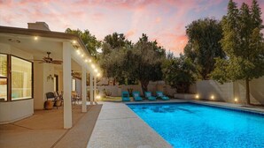A swimming pool with a covered patio area, outdoor seating, and trees in the background. - Beautiful 5-Bdrm Vacation Home W/Heated Pool ! (Scottsdale)