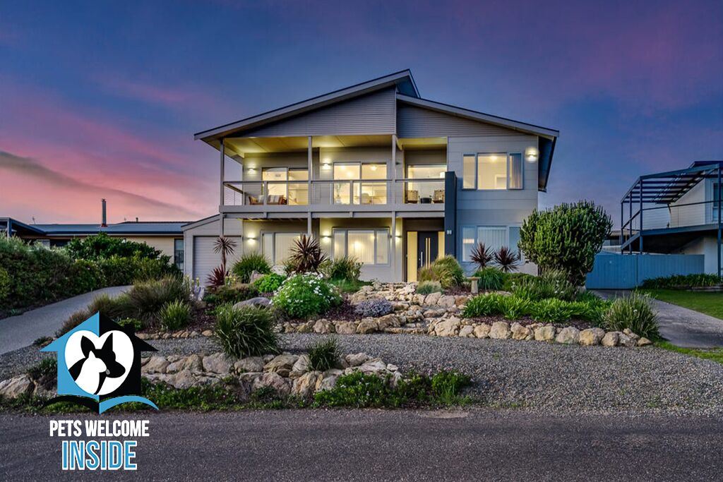 A modern two-story house with a well-maintained garden and a 'Pets Welcome Inside' sign.