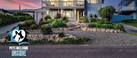A modern two-story house with a well-maintained garden and a 'Pets Welcome Inside' sign.