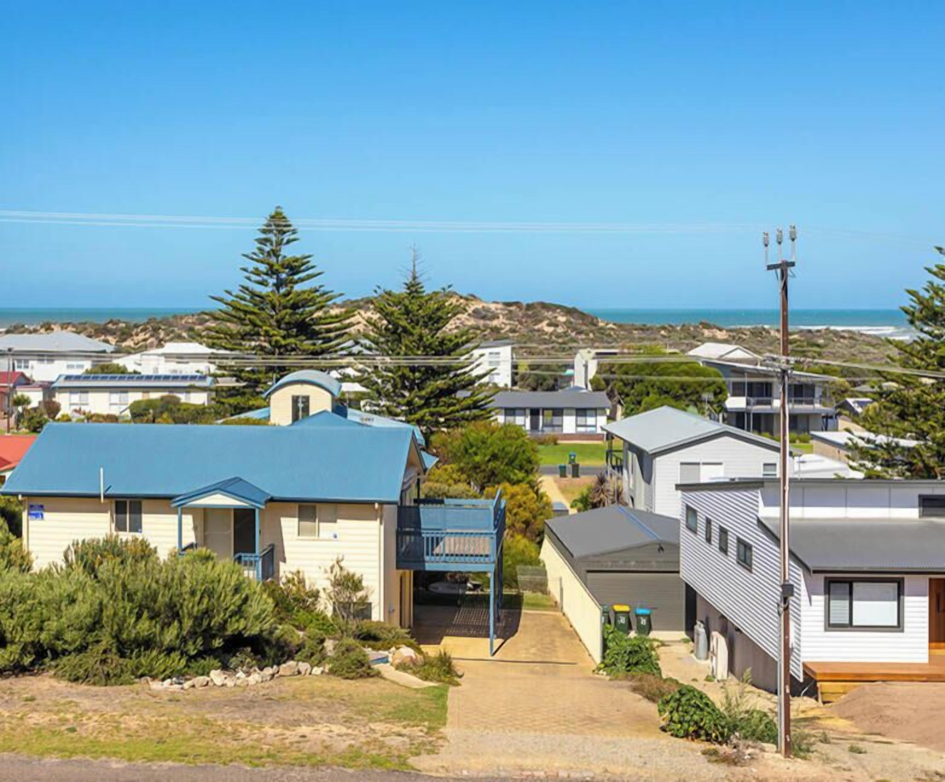 Un área residencial costera con casas, cielo despejado y vista al océano.
